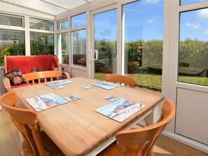A conservatory with a wooden table and chairs, large windows, and a red cushion on a chair. - 2 Bed in Alford (oc-92399) (Huttoft)