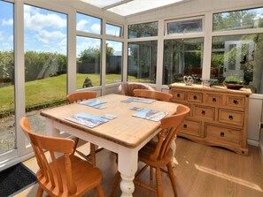 A conservatory with a wooden table and chairs, a dresser, and a view of the garden. - 2 Bed in Alford (oc-92399) (Huttoft)