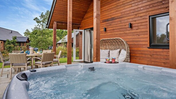 A hot tub with a wooden deck, wicker furniture, and a view of a house. - 3 Bed in Swansea (oc-91721) (Upper Killay)