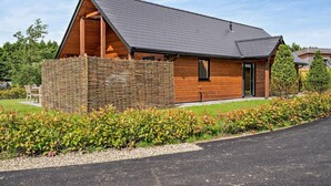 A modern house with a sloped roof, wooden exterior, and a stone wall. - 3 Bed in Swansea (oc-91721) (Upper Killay)