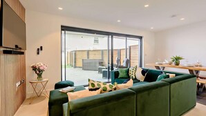 Una sala moderna con un sofá verde, una mesita redonda y un comedor con una mesa y sillas de madera.