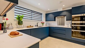Una cocina moderna con armarios azul oscuro, encimera blanca, horno de acero inoxidable y una ventana con persianas.