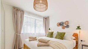 Un dormitorio con cama de madera, cortinas color beige, lámpara de fibra natural y decoración en la pared.