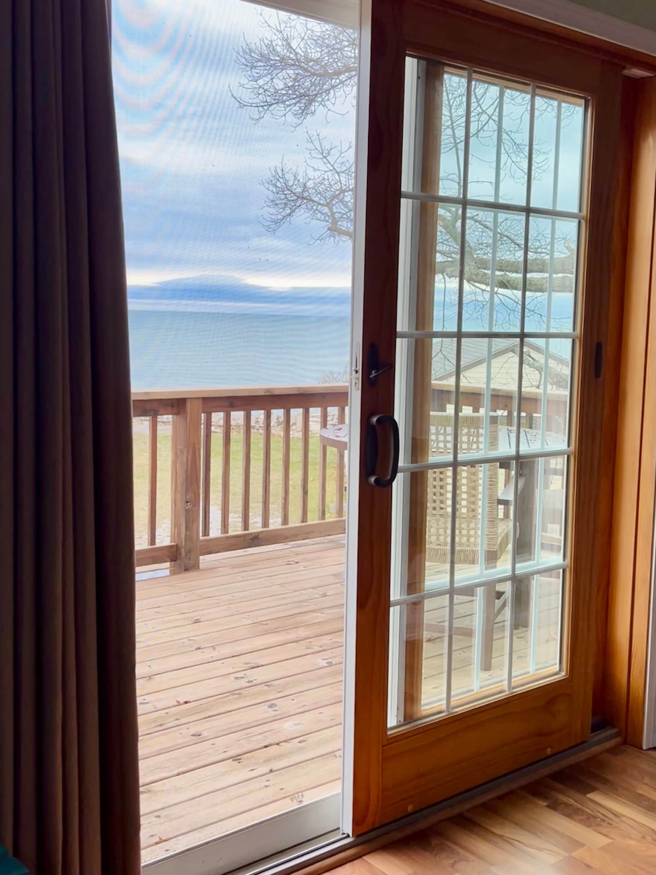 A wooden door with a glass panel leading to a deck with a view of a body of water.