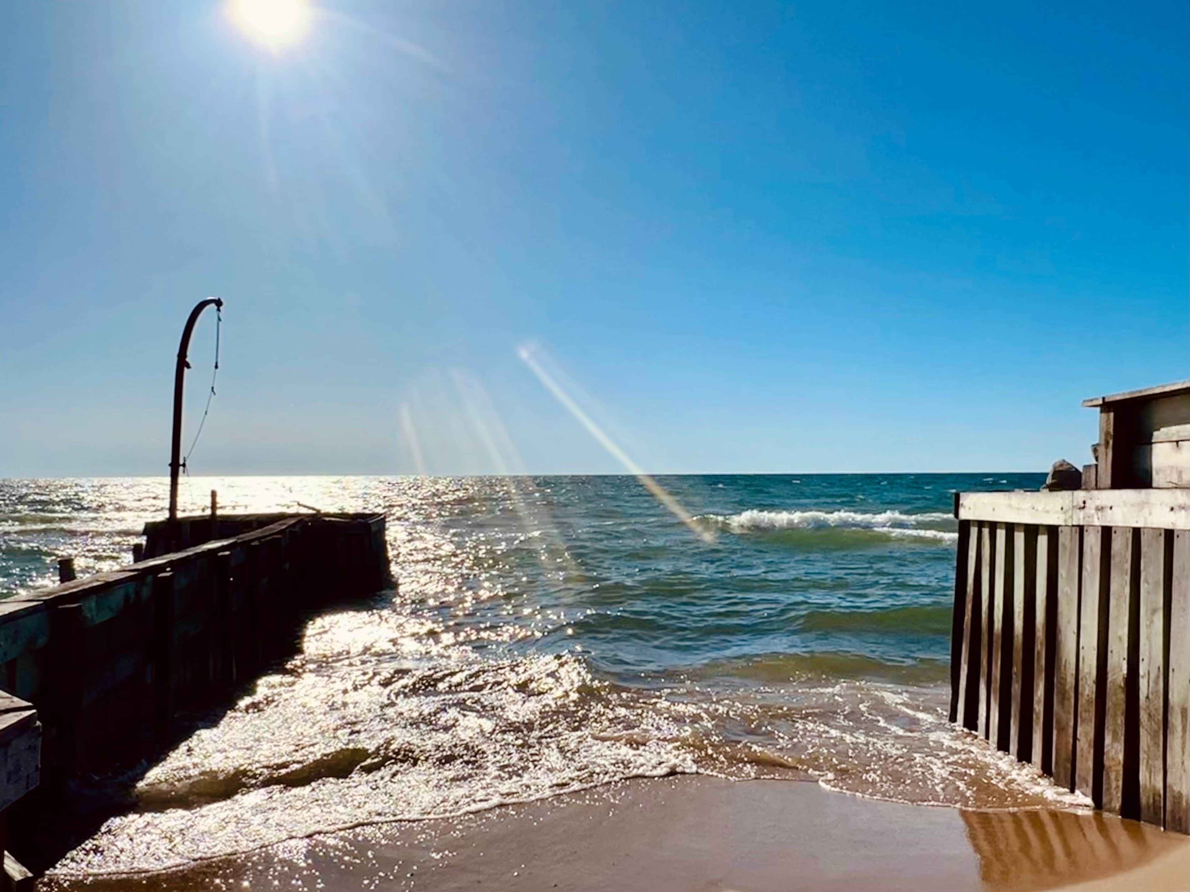 A pier extending into the sea with a clear sky and sunlight reflecting off the water.