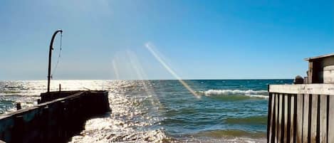 A pier extending into the sea with a clear sky and sunlight reflecting off the water.
