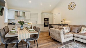 Une cuisine moderne avec des meubles blancs, une table à manger dressée avec des assiettes et des verres, et un canapé agrémenté de coussins à motifs floraux.