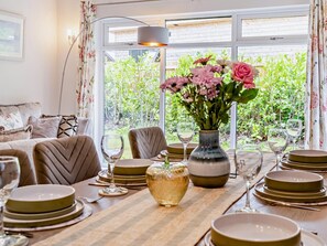 A dining area with a table set for four, a vase with flowers, and a view of greenery outside.