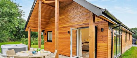 A wooden cabin with a covered patio, a hot tub, and a dining area.