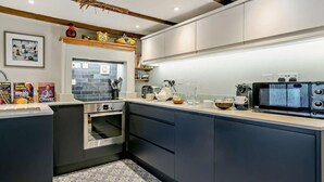 A modern kitchen with dark cabinetry, a built-in oven, a microwave, and a tiled backsplash. - 3 Bed in Truro (oc-91792) (Truro)