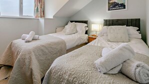 A bedroom with two beds, a window, a lamp, and a Cornwall poster. - 3 Bed in Truro (oc-91792) (Truro)