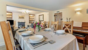 A dining room with a long table set for four, a piano, and a fireplace. - 3 Bed in Truro (oc-91792) (Truro)