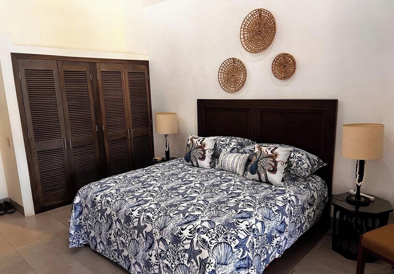 Une chambre à coucher avec un grand lit, deux tables de chevet avec des lampes, une armoire et trois éléments décoratifs fixés au mur.