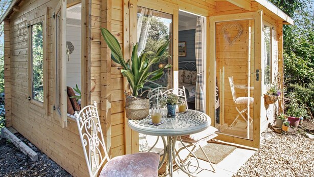 Una cabaña de madera con un pequeño patio, una mesa redonda de metal y sillas.