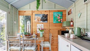 Una habitación acogedora de estilo cabaña con interior de madera, una mesa de comedor con sillas, un rincón de cocina y un ventanal con vistas a la vegetación.