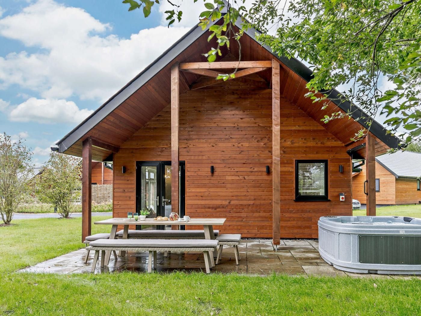 Eine Holzdiele mit überdachter Terrasse, einem Whirlpool und einem Picknicktisch mit Bänken.