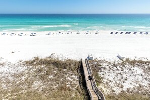 Une plage de sable blanc, une promenade en bois et des parasols de plage.