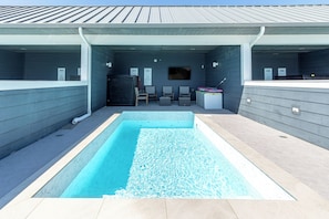 En swimmingpool med ett kaklat poolområde, en överbyggd sittplats med stolar och en tv-skärm.