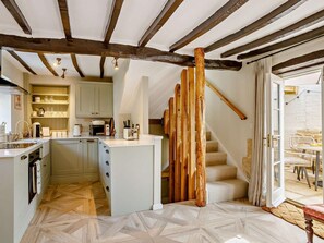 A kitchen with a central island, wooden beams, and a staircase leading to a balcony. - 1 Bed in Stamford (oc-92406) (Ketton)