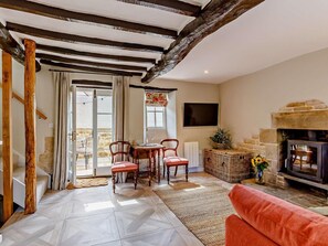 Un salon chaleureux avec une cheminée, un coin repas avec des chaises et une table, et un escalier avec des poutres en bois.