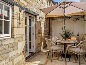 A stone building with a patio area featuring wicker chairs, a table with plates and glasses, and a large umbrella. - 1 Bed in Stamford (oc-92406) (Ketton)