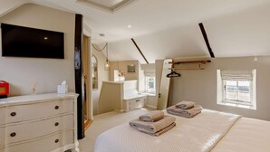 Quarto com cama, cômoda, espelho e televisão fixada na parede.