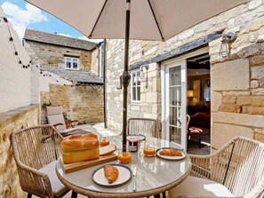 A dining area with wicker chairs, a round table, and a large umbrella. - 1 Bed in Stamford (oc-92406) (Ketton)