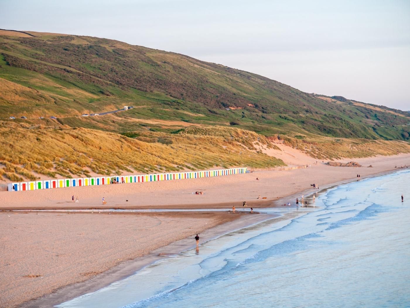 Une plage bordée d’une rangée de tentes colorées, une plage de sable et, en arrière-plan, une colline couverte d’herbe.