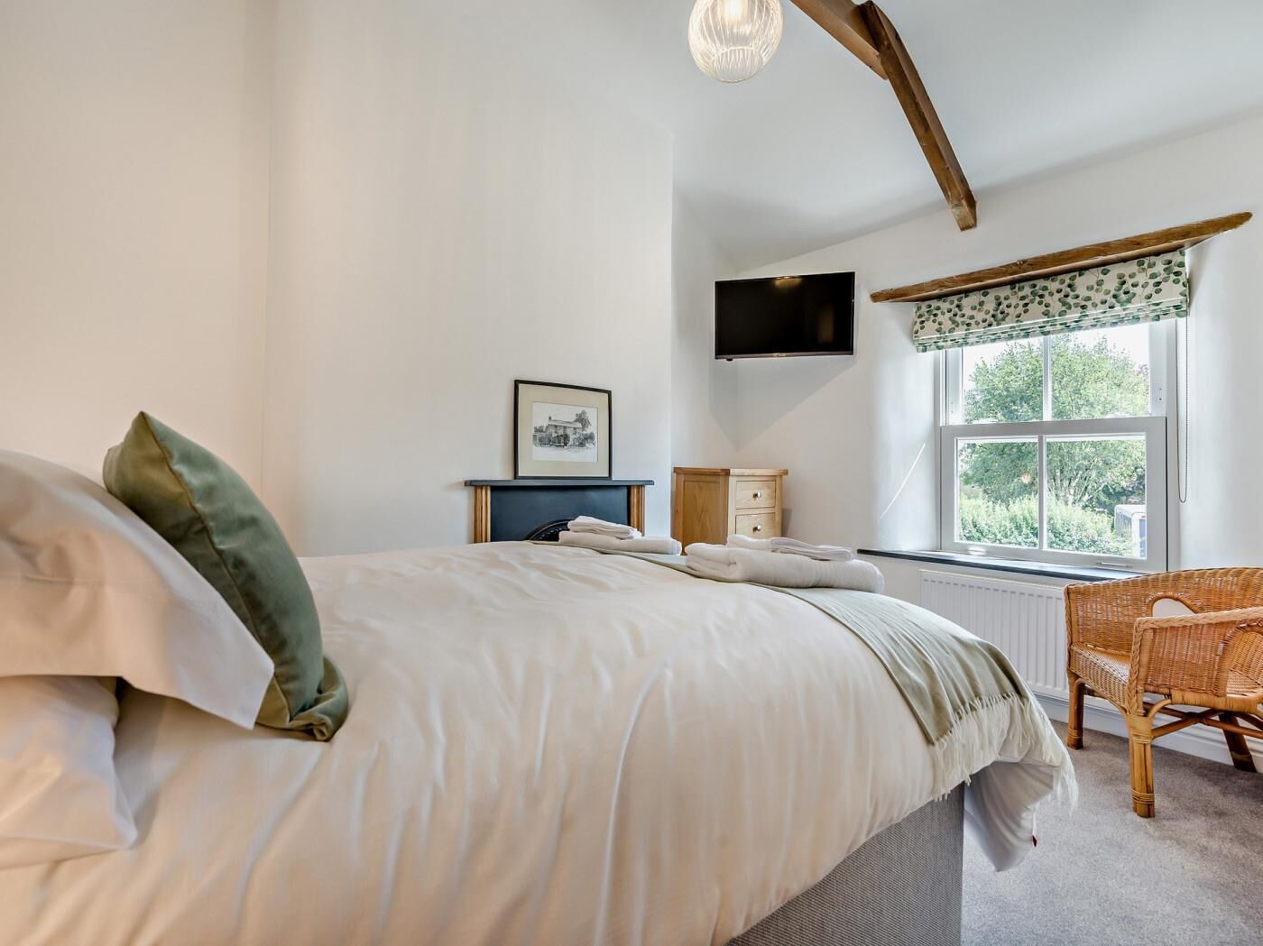 A bedroom with a bed, a television, a window with a view, a chair, and a picture on the wall.