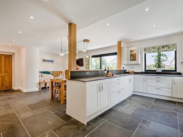 Una cocina moderna con armarios blancos, una isla central y un comedor con mesa y sillas de madera.