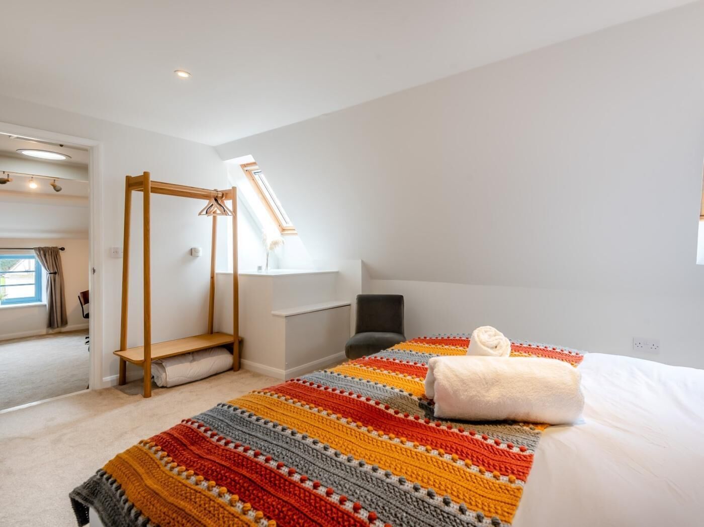 A bedroom with a wooden canopy bed, a colorful striped blanket, a white pillow, and a view of a window and another room.