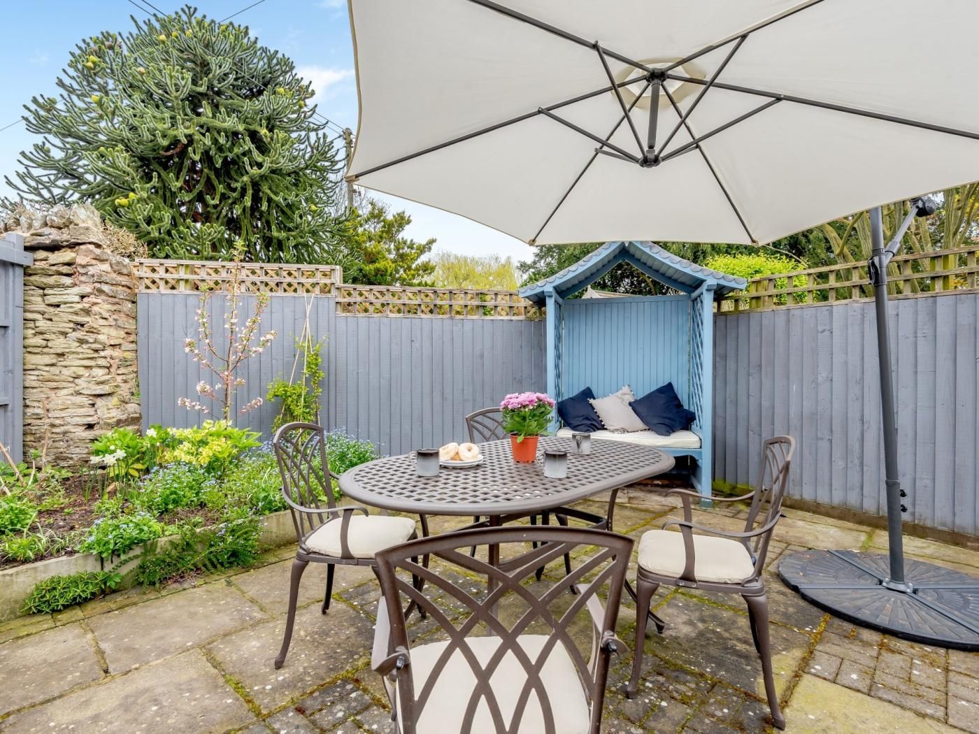 An outdoor patio with a round table, chairs, and a blue garden bed.