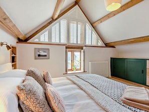 A bedroom with a sloped ceiling, a bed with multiple pillows, a window with blinds, a radiator, and a green cabinet.
