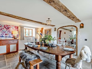 A dining area with a wooden table set for four, a large mirror, and a rustic ceiling beam.