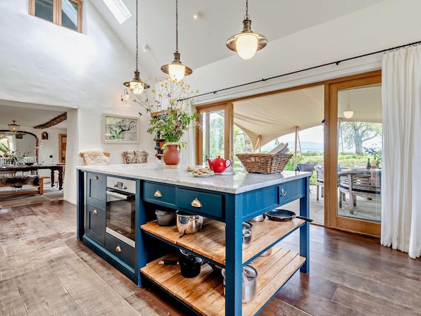 A kitchen with a central island, wooden shelves, and hanging pendant lights.