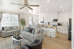 A modern living room with a grey sofa, a coffee table, and a grey armchair. There is a kitchen area with white cabinets and a microwave. - Heated Pool, PickleBall - New & Beautiful - Save Today (Washington)