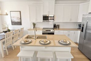 A modern kitchen with white cabinetry, a stainless steel refrigerator, and a central island with seating. - Heated Pool, PickleBall - New & Beautiful - Save Today (Washington)