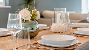 Een eettafel gedekt met witte borden, glazen en een vaas met witte bloemen.
