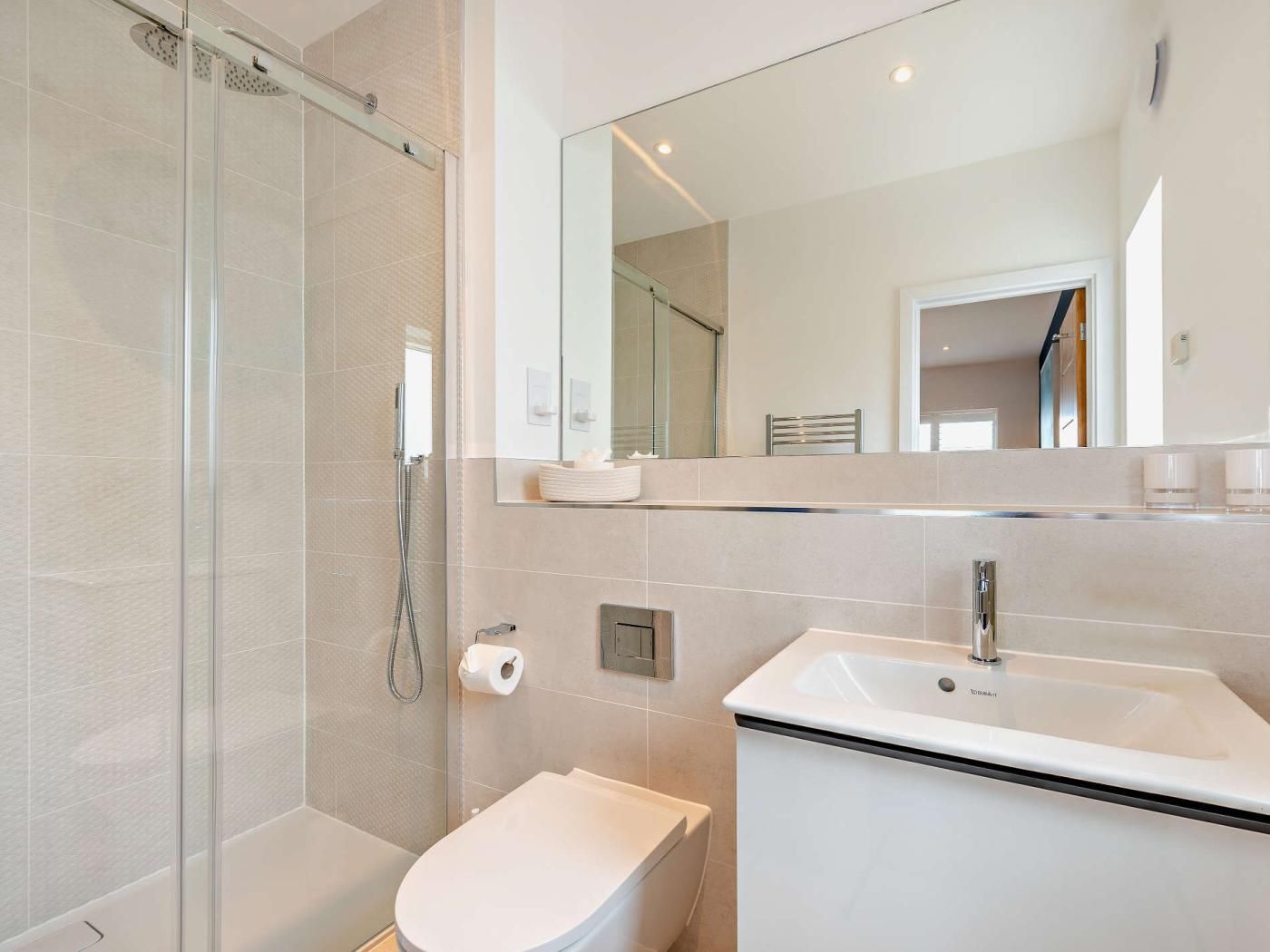 A modern bathroom with a glass-enclosed shower, a white toilet, and a sink with a mirror above.