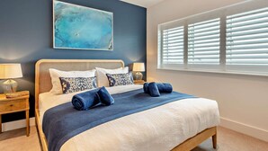 Een slaapkamer met een bed, twee nachtkastjes, een raam met zonwering en een abstract schilderij aan de muur.