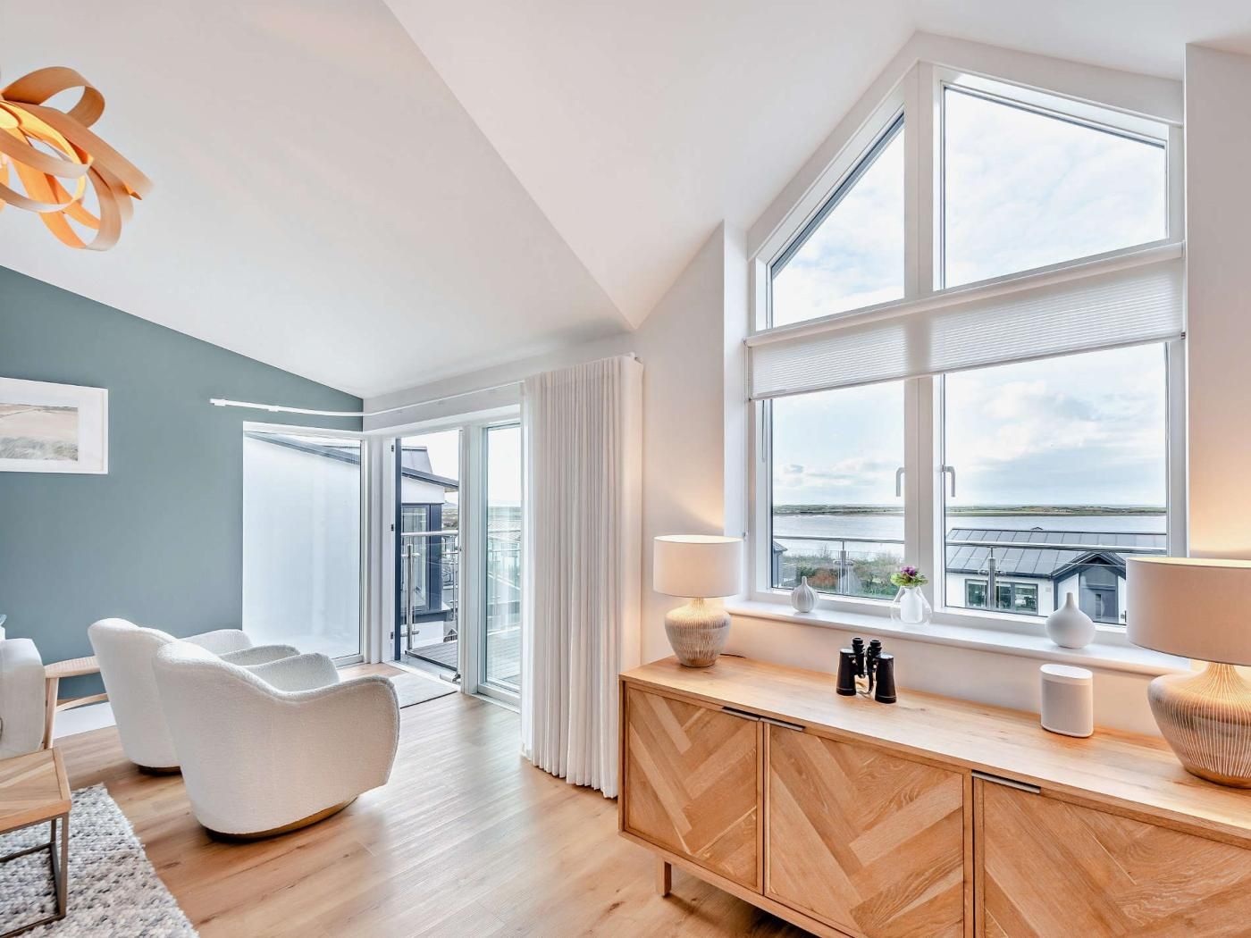 Una habitación moderna con un ventanal grande, un armario de madera y una silla blanca.