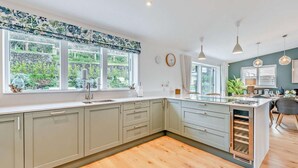 Een moderne keuken met een groot eiland, een geïntegreerde wijnkoeler en uitzicht op de tuin door grote ramen.