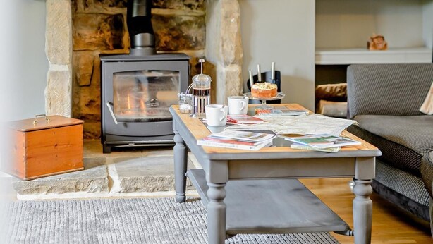Ett mysigt vardagsrum med en öppen spis i sten, ett soffbord med tidningar och en bekväm soffa.