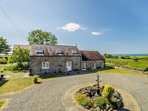A stone farmhouse with a gravel driveway, a circular stone fountain, and a view of the sea. - 4 Bed in Llanrhystud (oc-92072) (Llanrhystyd)