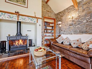 A cozy living room with a fireplace, a leather sofa, a glass coffee table, and a stone wall. - 4 Bed in Llanrhystud (oc-92072) (Llanrhystyd)