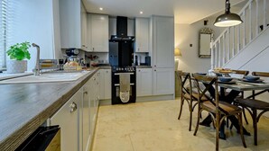 Une cuisine moderne avec des meubles blancs, une cuisinière noire et un coin repas doté de chaises en bois.