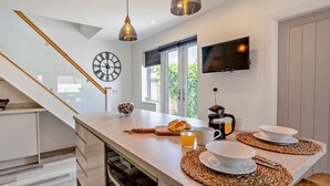 Een moderne keuken met een centraal eiland, een klok, een koffiezetapparaat en een televisie aan de wand.