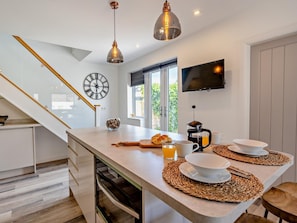 A modern kitchen with a central island, a clock, a coffee maker, and a TV mounted on the wall. - 2 Bed in Poulton-le-fylde (oc-92095) (Knott End-on-Sea)