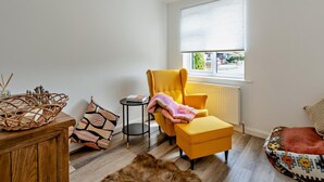 Een kamer met een gele fauteuil, een klein rond tafeltje, een rieten mand en een kamerkleed met dessin.