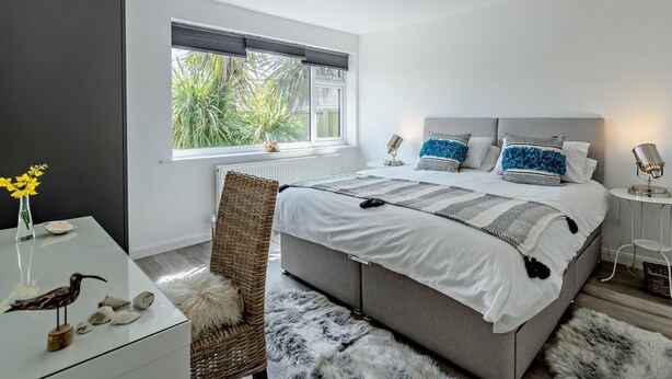 Een moderne slaapkamer met een groot bed, een nachtkastje, een stoel en uitzicht op groen.